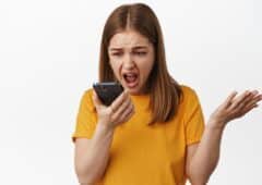 Angry girl shouting at smartphone voice message, talk on speakerphone and screaming at mobile phone dynamic, shaking hands frustrated, standing against white background